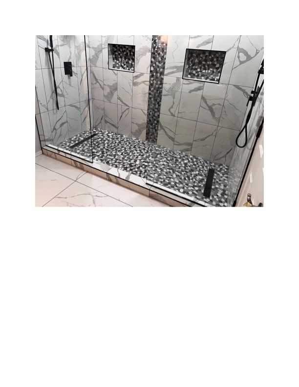 A walk in shower with a glass door and a pebble floor.