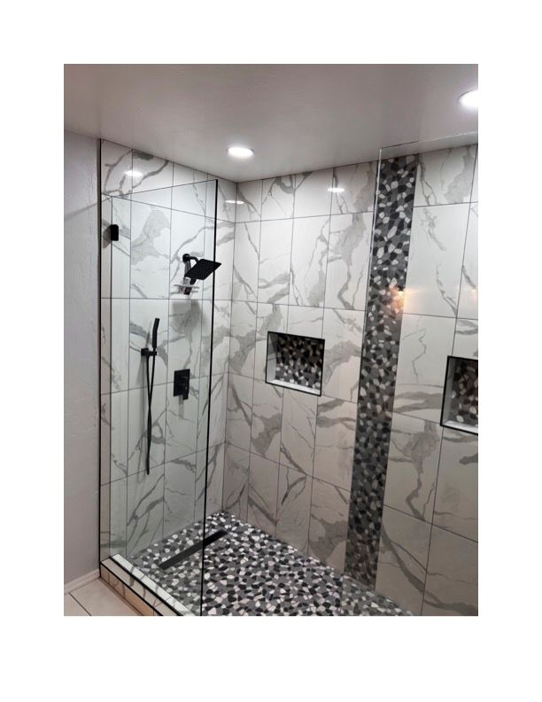 A bathroom with marble tiles and a walk in shower with a glass door.