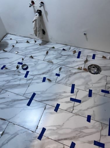 A bathroom floor with tiles and blue tape on it.