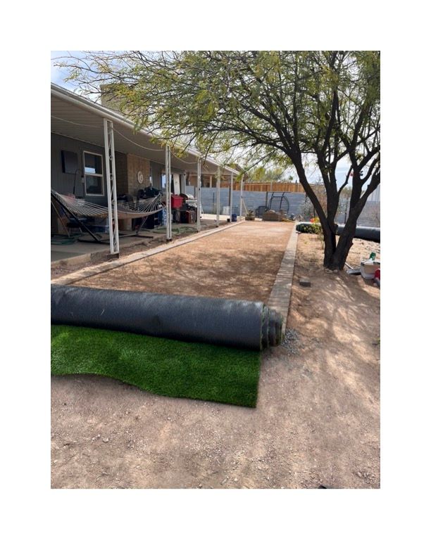A roll of artificial grass is being rolled out in front of a house. Turf is installed