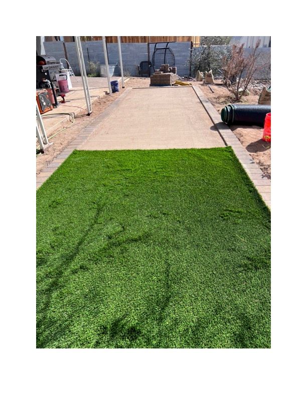 A large piece of artificial grass is sitting on top of a dirt road. Turf is installed