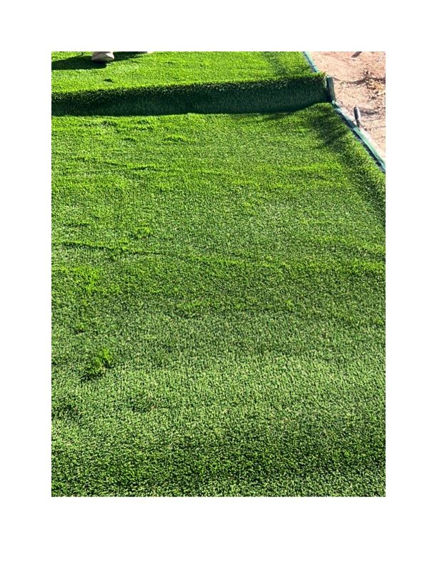 A close up of a lush green lawn with a path in the background. Turf is installed