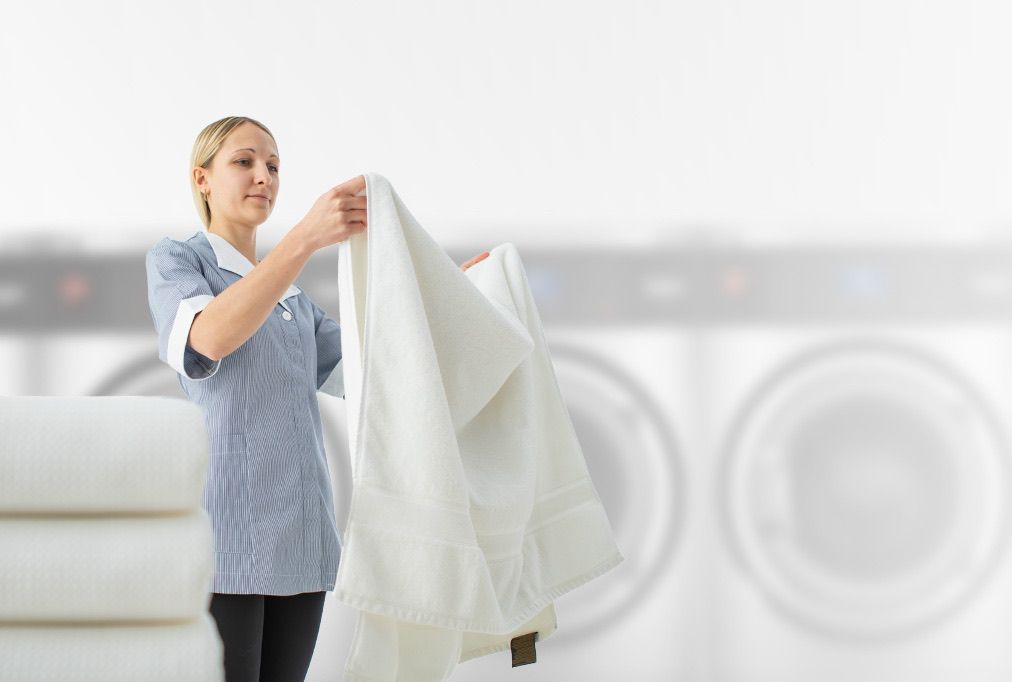 A woman is holding a white towel in front of a washing machine.