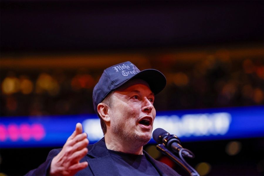 Elon musk is wearing a hat and speaking into a microphone.