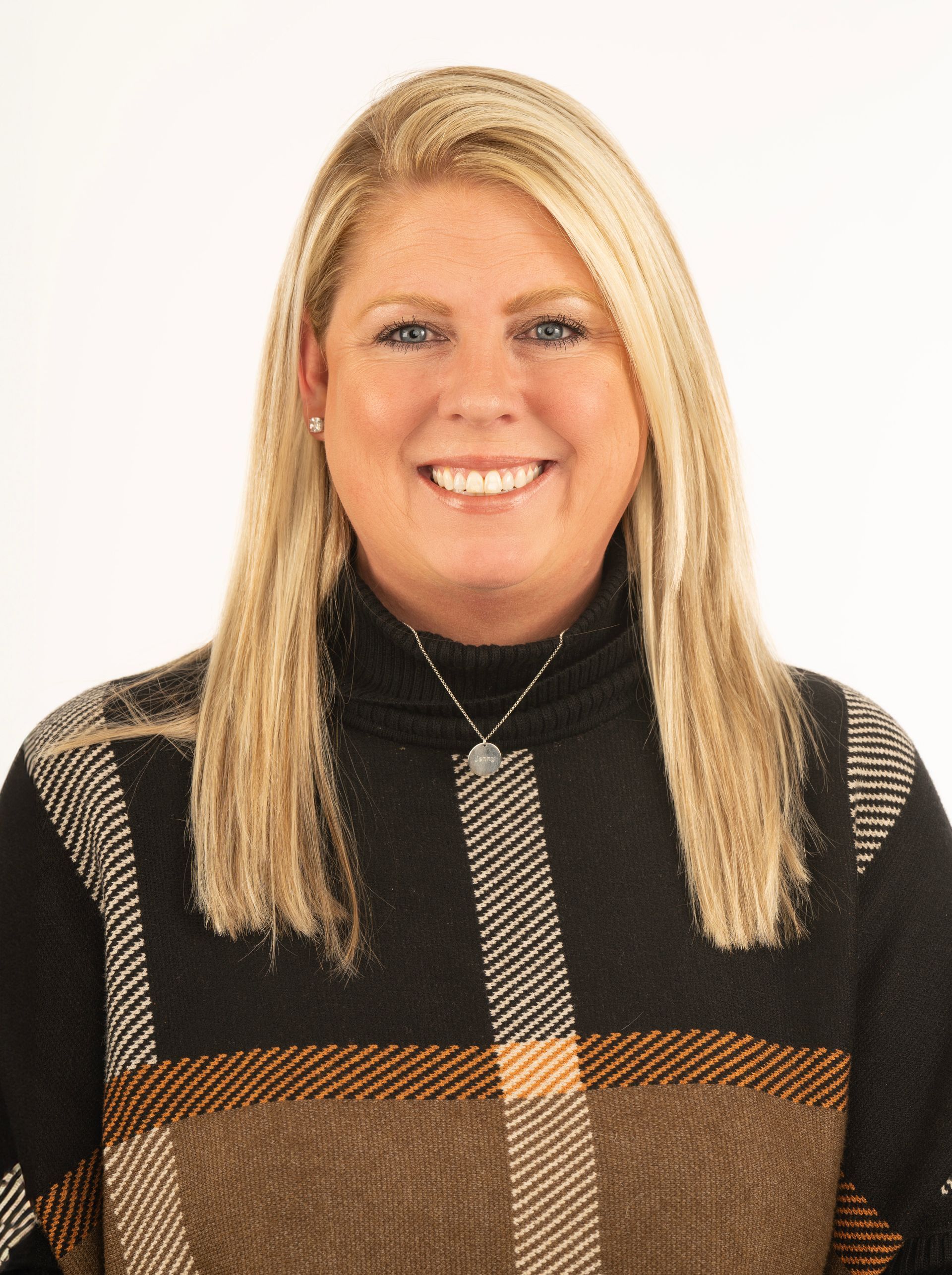 A woman wearing a plaid sweater and a necklace is smiling for the camera.