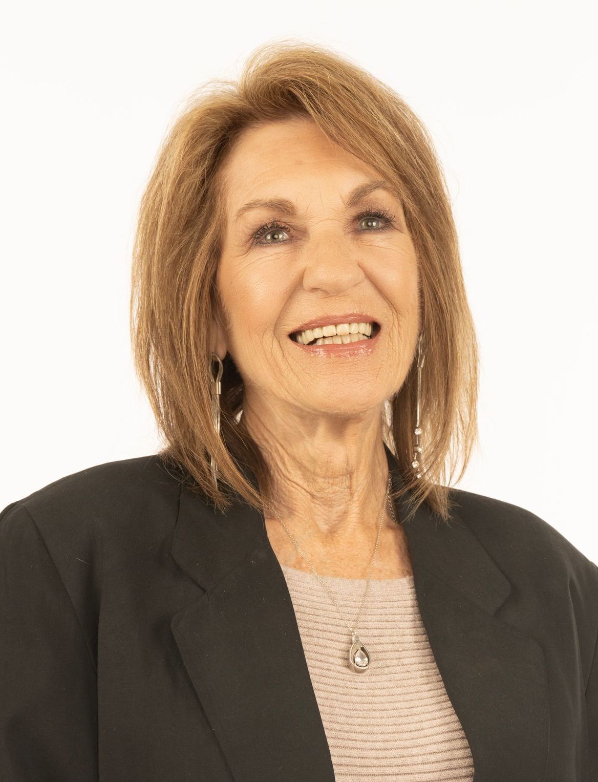 A woman wearing a black jacket and a necklace is smiling.