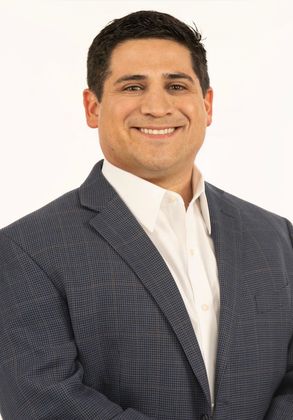 Attorney Will Ortiz in a suit and white shirt is smiling for the camera.
