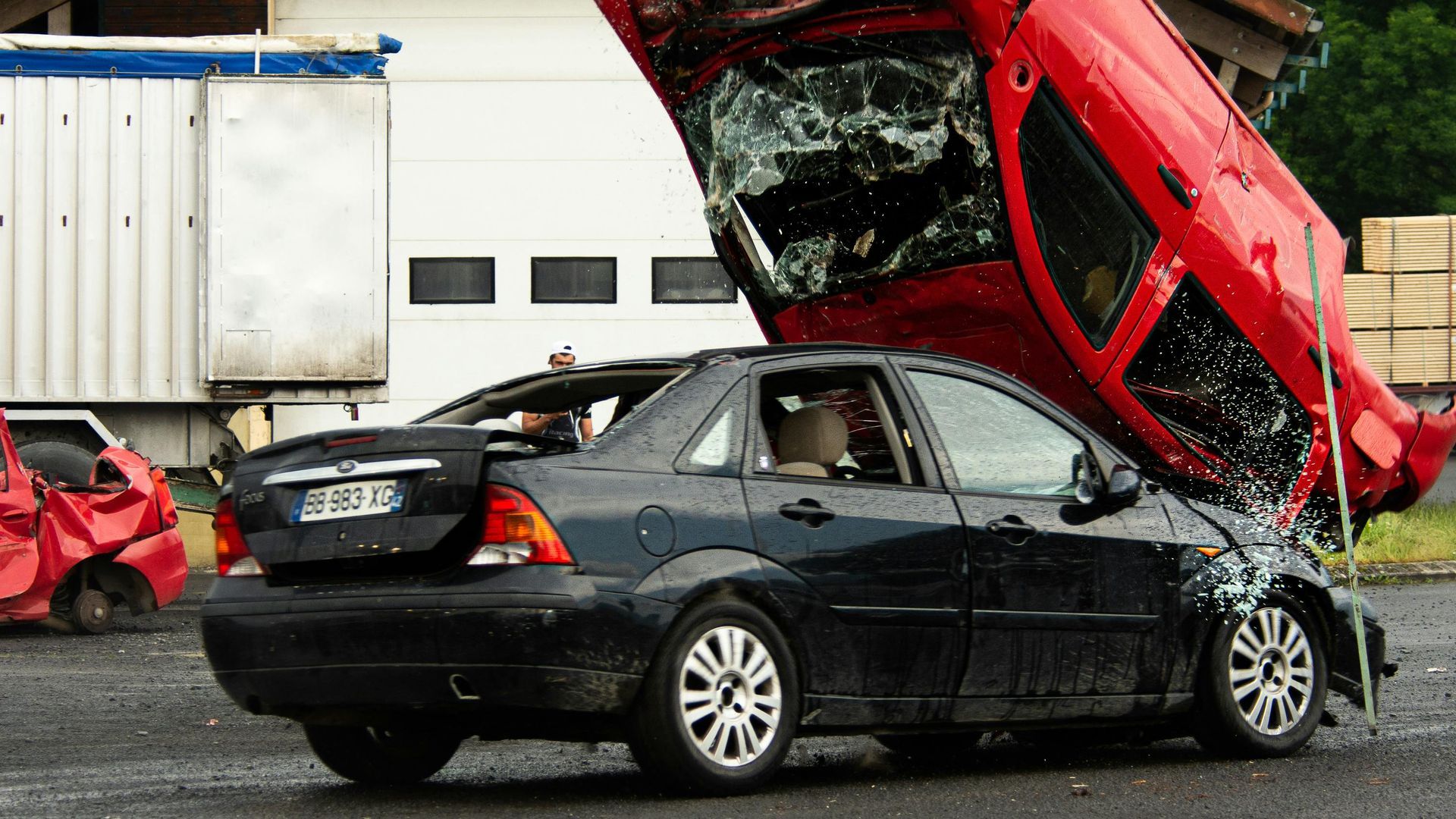 A woman is looking at her cell phone in front of a damaged car.
