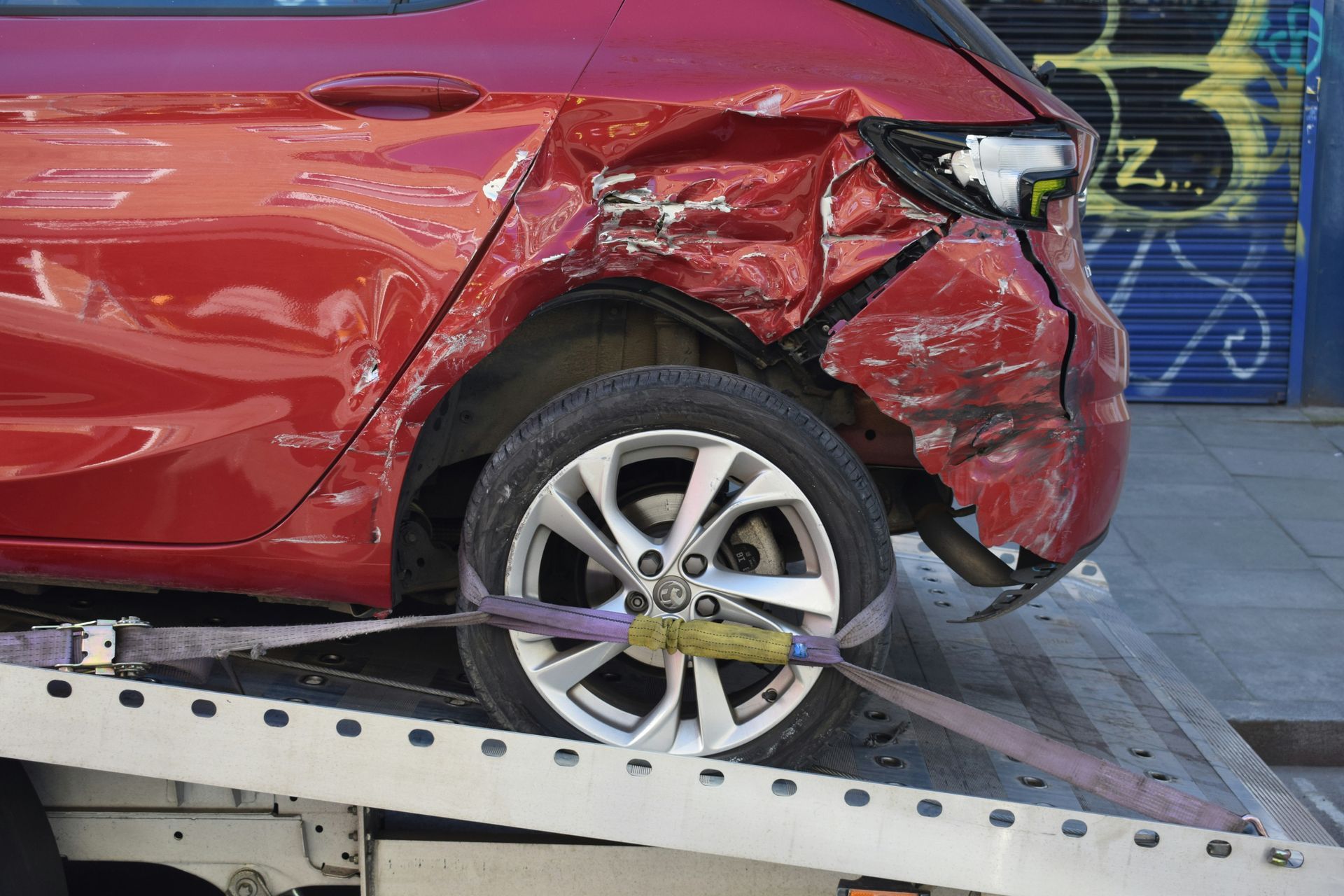 A woman is looking at her cell phone in front of a damaged car.