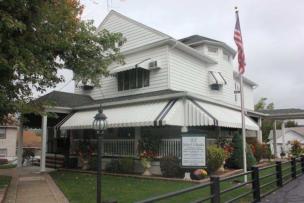 White house with black-striped awnings, garden, and American flag on a rainy street corner.