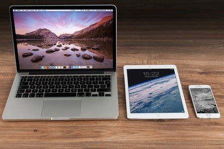 A laptop , tablet , and cell phone are sitting on a wooden table.