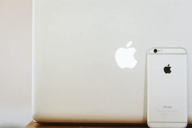 An iphone is sitting next to an apple laptop on a table.