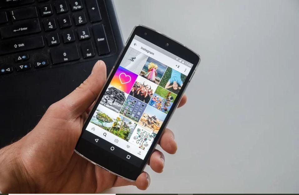 A person is holding a cell phone in their hand in front of a laptop.