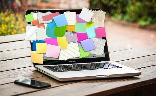 A laptop with sticky notes on it is sitting on a wooden table.