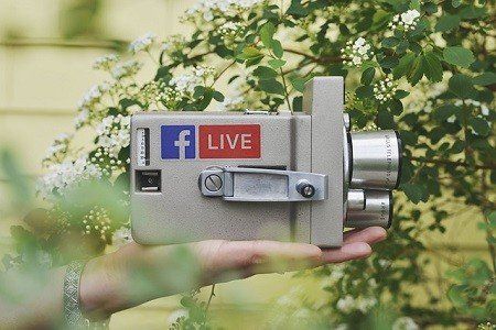 A person is holding a camera with a facebook live sticker on it.