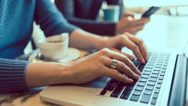 A person is typing on a laptop computer with a cup of coffee in the background.