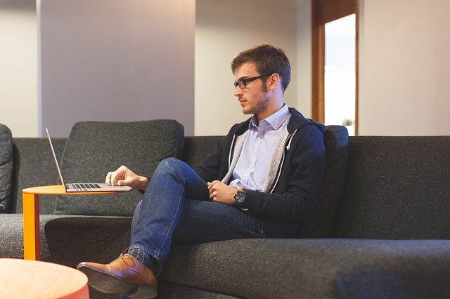 A man is sitting on a couch using a laptop computer.