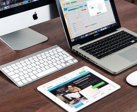 A laptop computer , tablet , keyboard and mouse are on a wooden table.