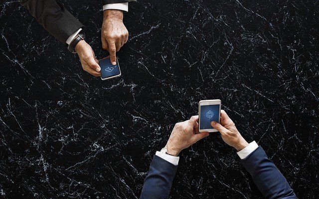 Two men are sitting at a table looking at their phones.