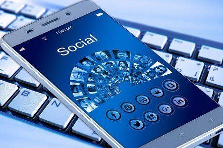 A cell phone with the word social on the screen is sitting on top of a keyboard.