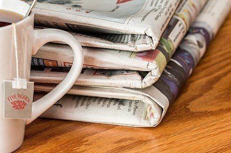 A cup of tea and a stack of newspapers on a wooden table.