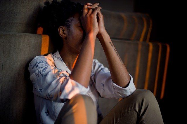 A woman is sitting on the ground with her hands on her face.