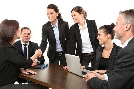 A group of business people are sitting around a table shaking hands.