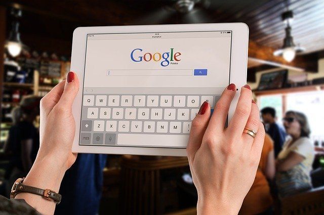 A woman is holding a tablet with a google search bar on the screen.