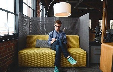 A man is sitting on a yellow couch looking at his phone.