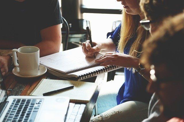 A group of people are sitting at a table with a laptop and notebooks.