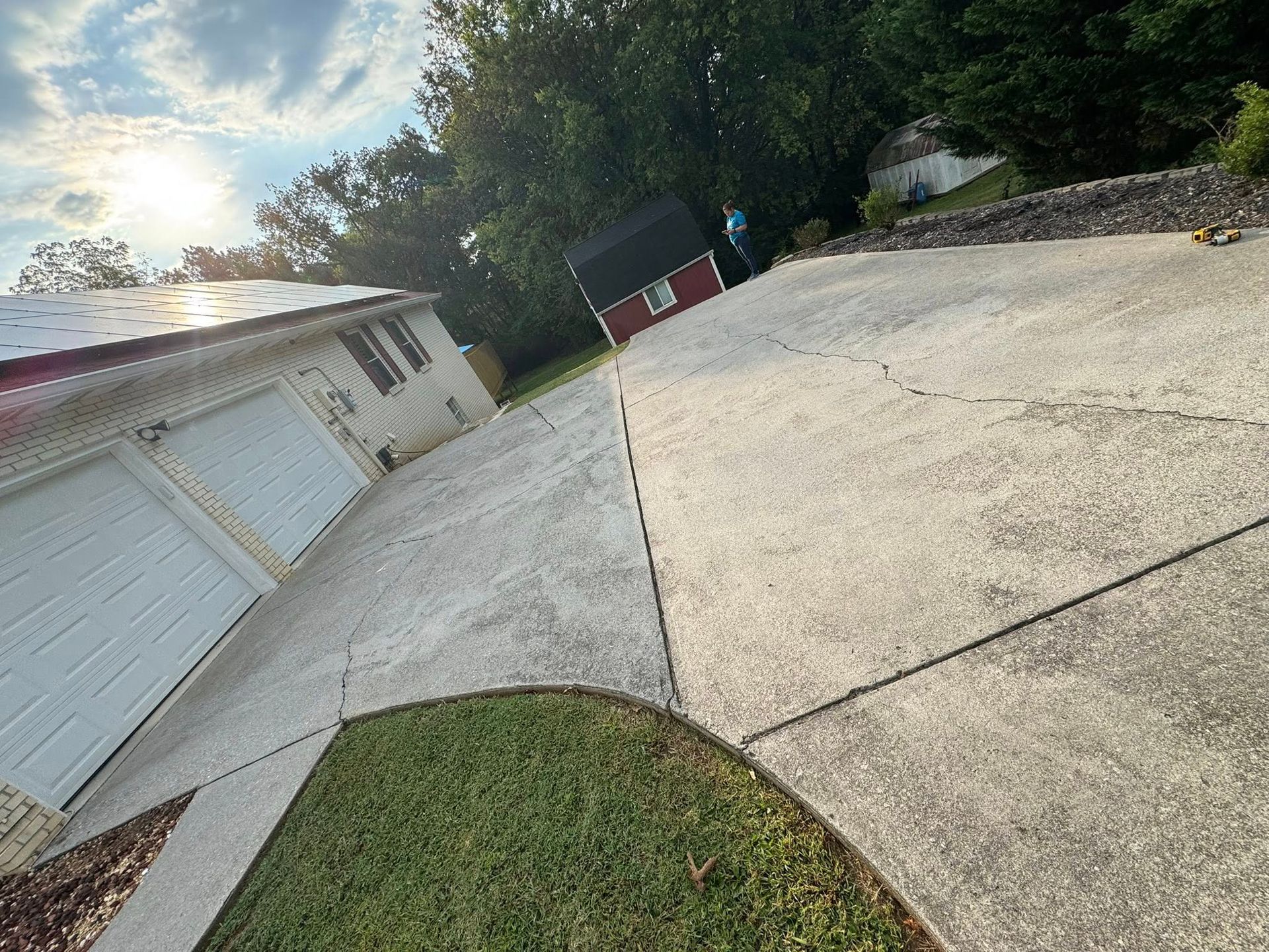Driveway leads to a garage and small red shed, sunny day.