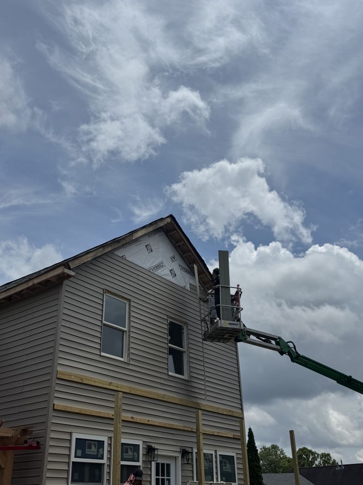 Construction workers on a lift installing siding on a two-story house under a cloudy sky.