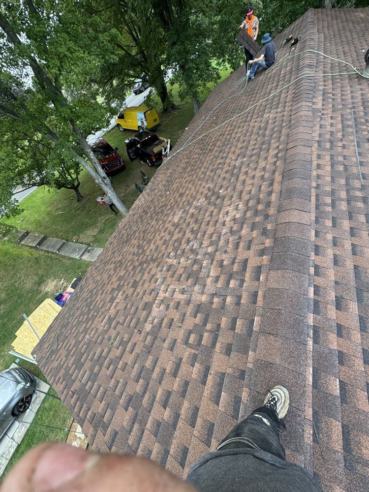 Workers installing brown asphalt shingles on a roof. One person in frame.