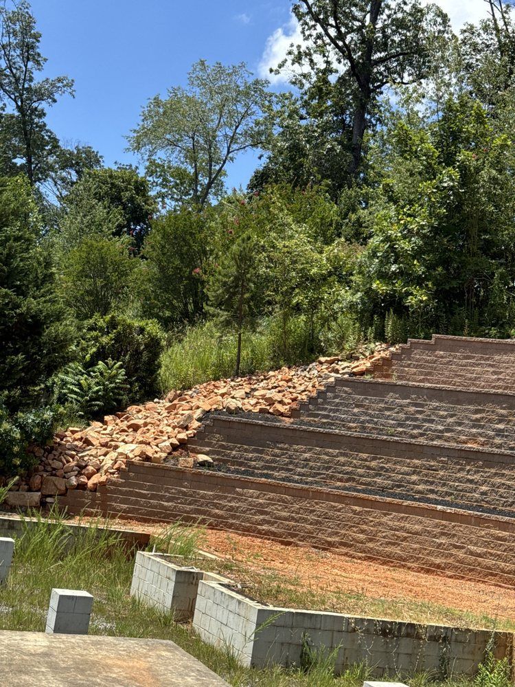 Hillside with tiered retaining walls; some bricks collapsed, surrounded by trees.