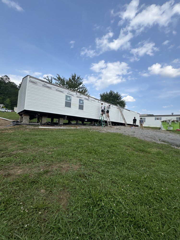 Mobile classroom on blocks; workers on ladder, green grass and blue sky background.