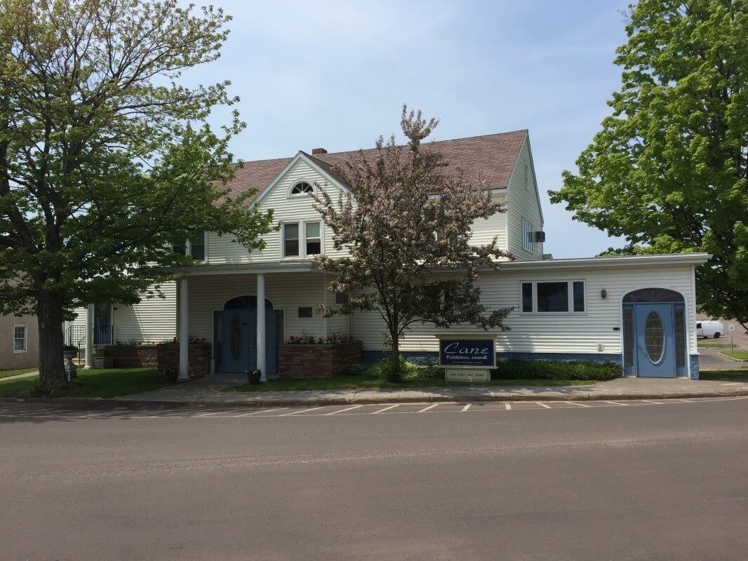 White two-story building with a brown roof and a small sign out front, under a blue sky.