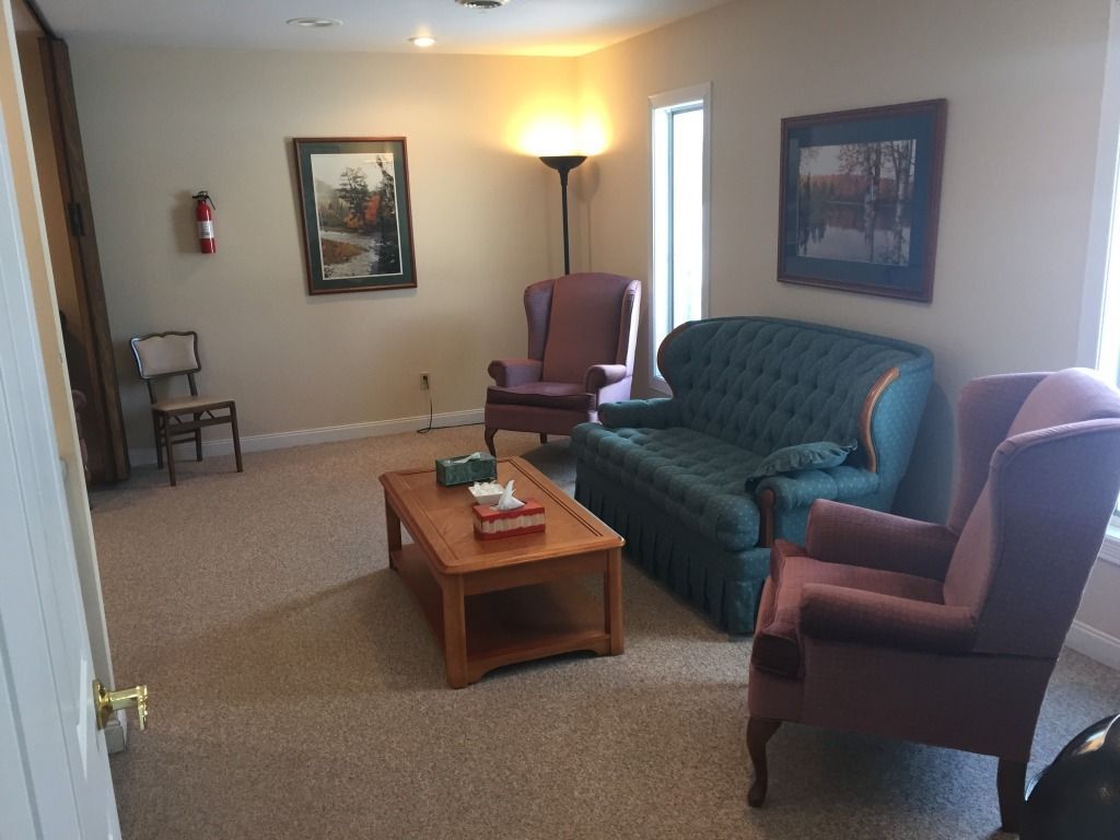 Cozy living room with armchairs, sofa, and a coffee table, artwork on walls, and a fire extinguisher.