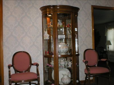 Wooden display cabinet with assorted items and two upholstered chairs.
