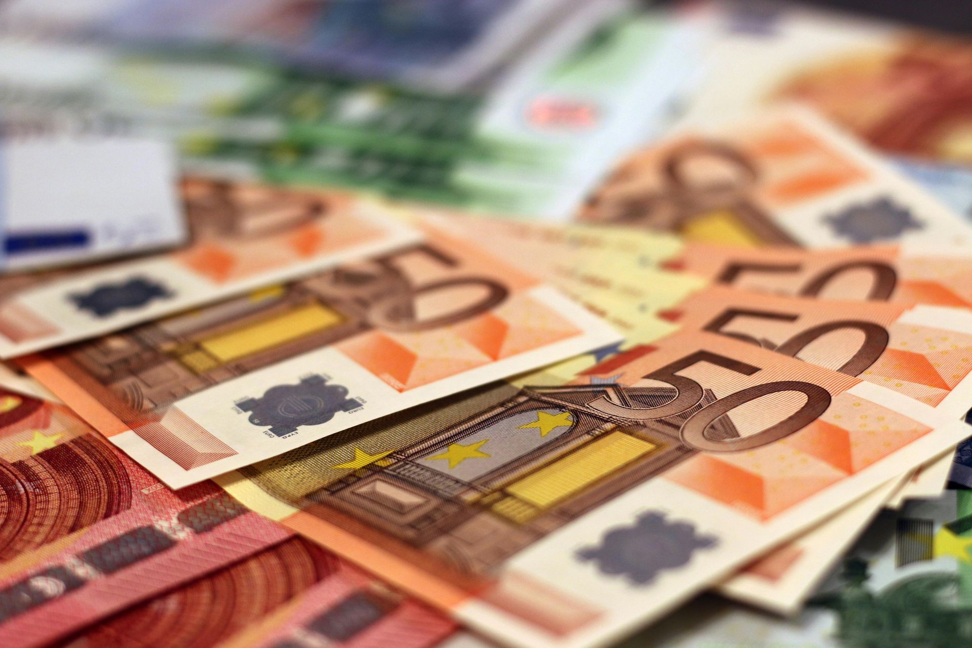 Billetes de euro, en su mayoría de 50, dispersos sobre una superficie. Predominan los tonos naranja y amarillo.