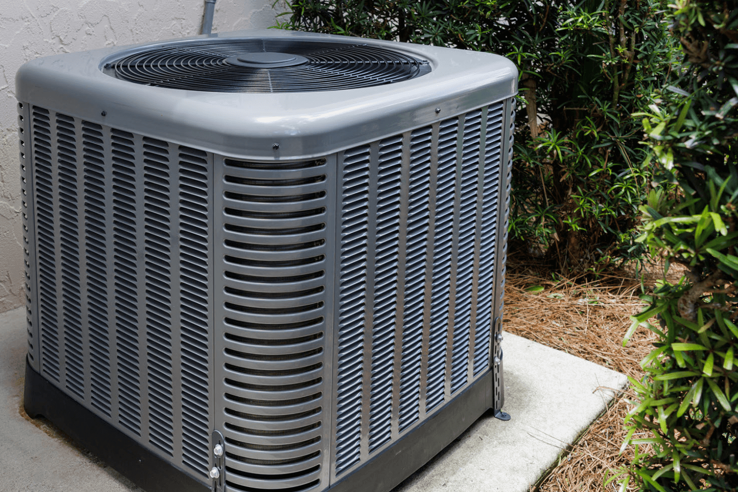 A large air conditioner is sitting on a sidewalk next to a bush.
