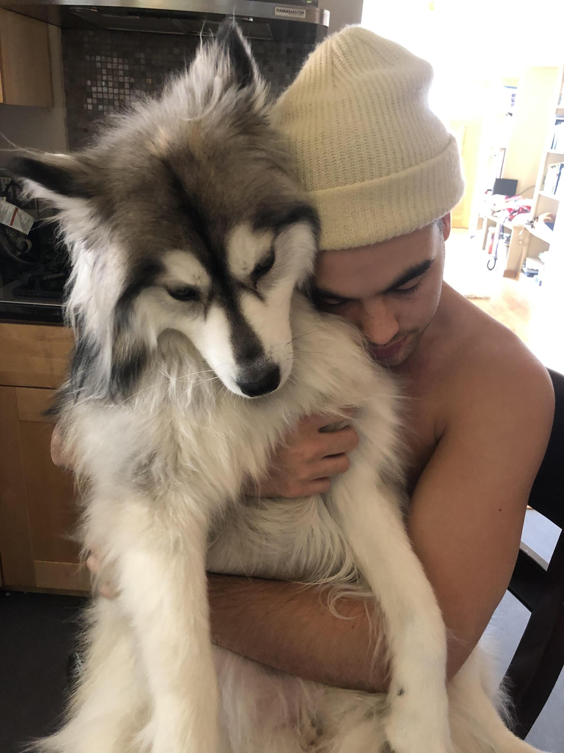 A shirtless man is holding a husky dog in his arms