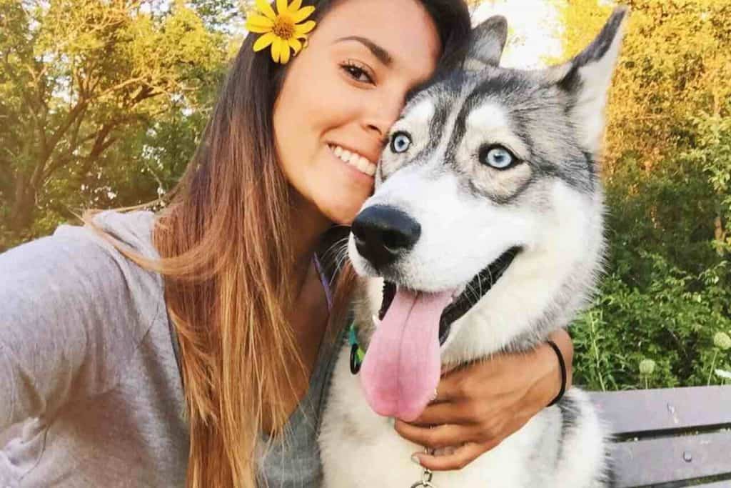A woman with a flower in her hair is hugging a husky dog