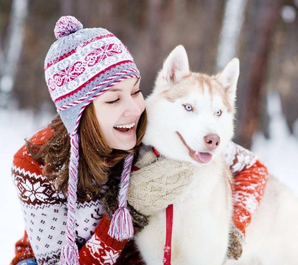 A woman is holding a husky dog in the snow