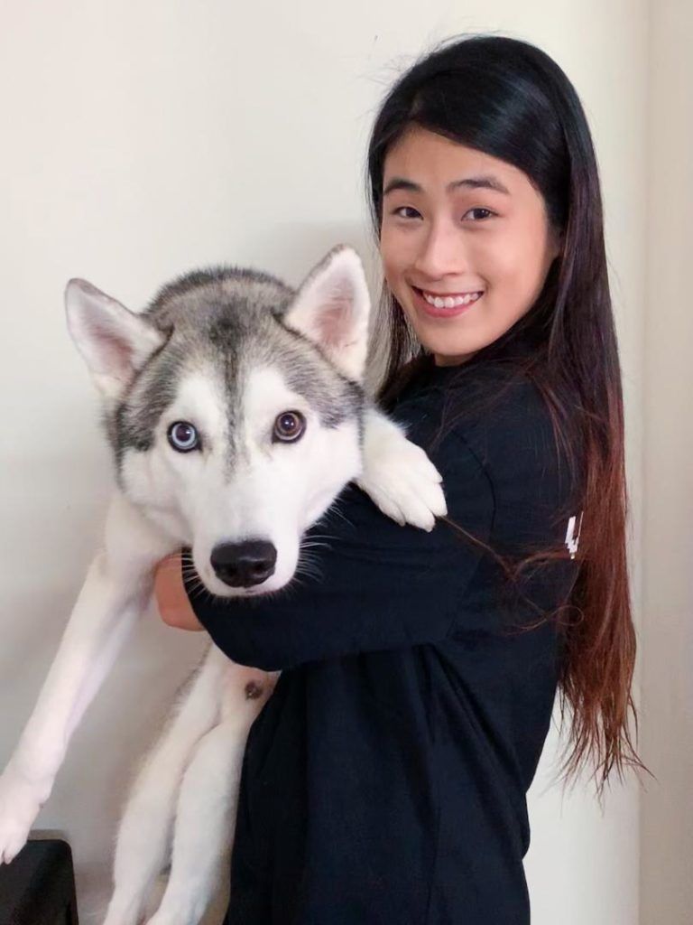 A woman is holding a husky dog in her arms.