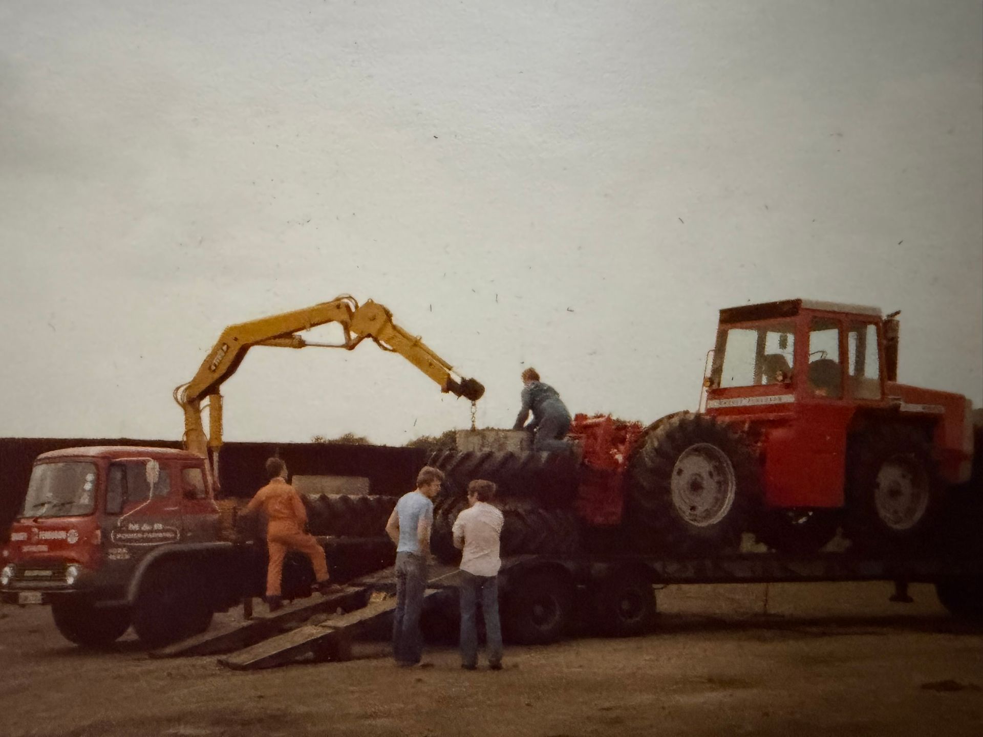 Truck loading tractor tires with a crane. Men working outside on a flatbed trailer.