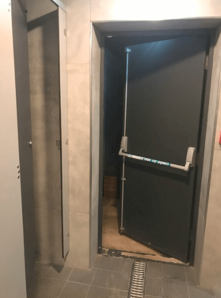 Gray fire exit door with panic bar, open in a hallway.