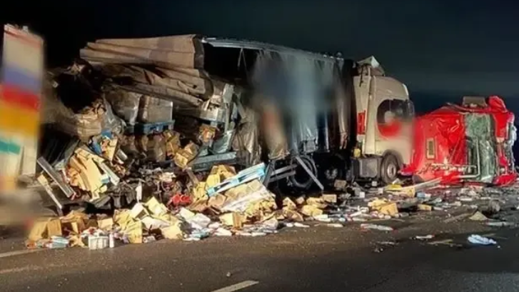 Severe truck accident scene at night; two vehicles heavily damaged, debris scattered on road.