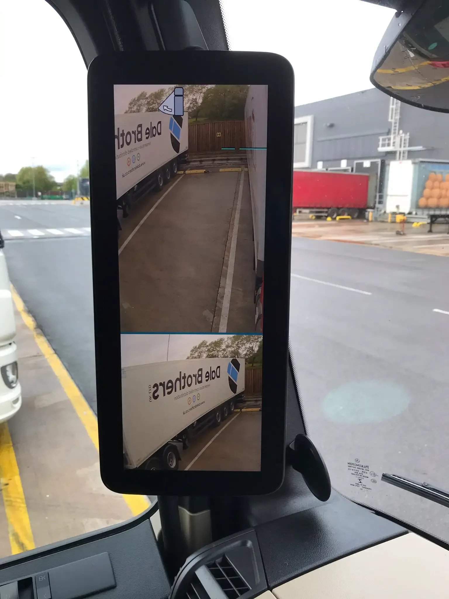 Rearview monitor inside truck cab showing split views of a trailer backing up in a paved area.