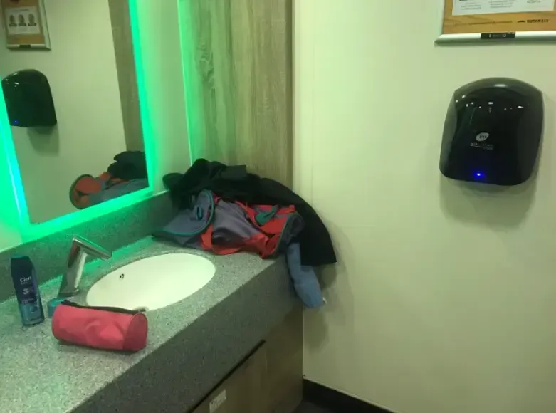 Bathroom with sink, mirror, hand dryer, and clothes. Green-lit mirror and granite counter.