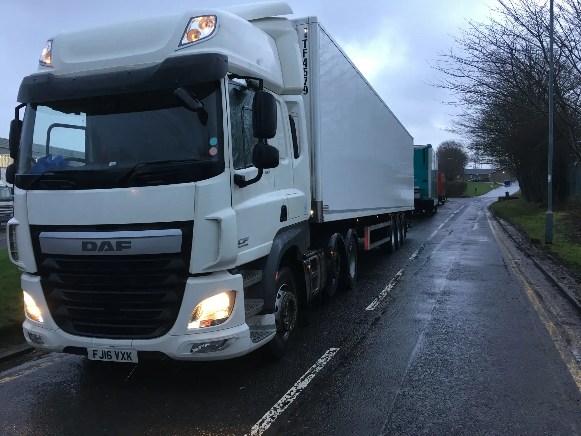 White DAF semi-truck on a wet road, cloudy sky.